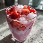 Close-up of a glass filled with the Copycat Starbucks Pink Drink, showing pink liquid, ice cubes, and fresh strawberry slices.