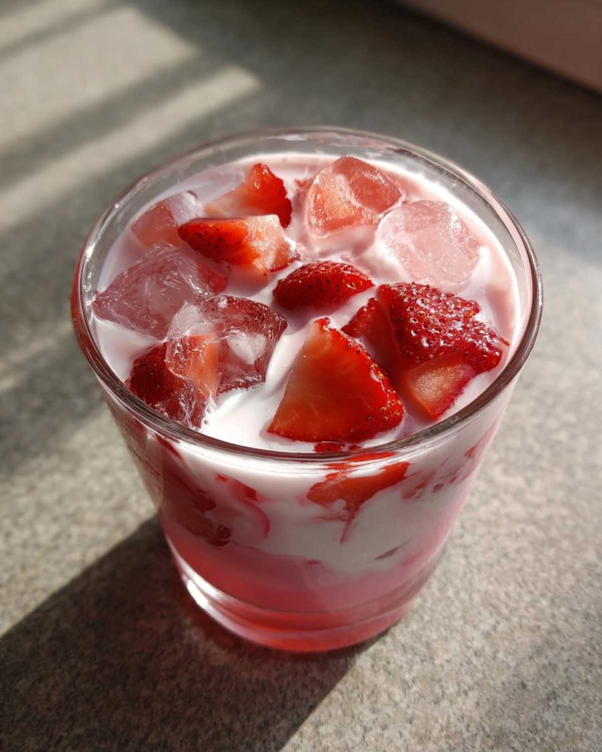 Close-up of a glass containing the Copycat Starbucks Pink Drink, showing layers of pink liquid, white coconut milk, ice cubes, and fresh strawberry pieces.