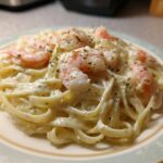 A close-up of Creamy Alfredo Shrimp Pasta with Garlic featuring fettuccine coated in rich white sauce and topped with pink shrimp and herbs.