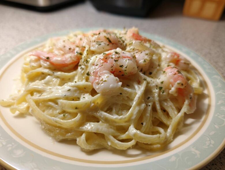 A close-up of Creamy Alfredo Shrimp Pasta with Garlic featuring fettuccine coated in rich white sauce and topped with pink shrimp and herbs.