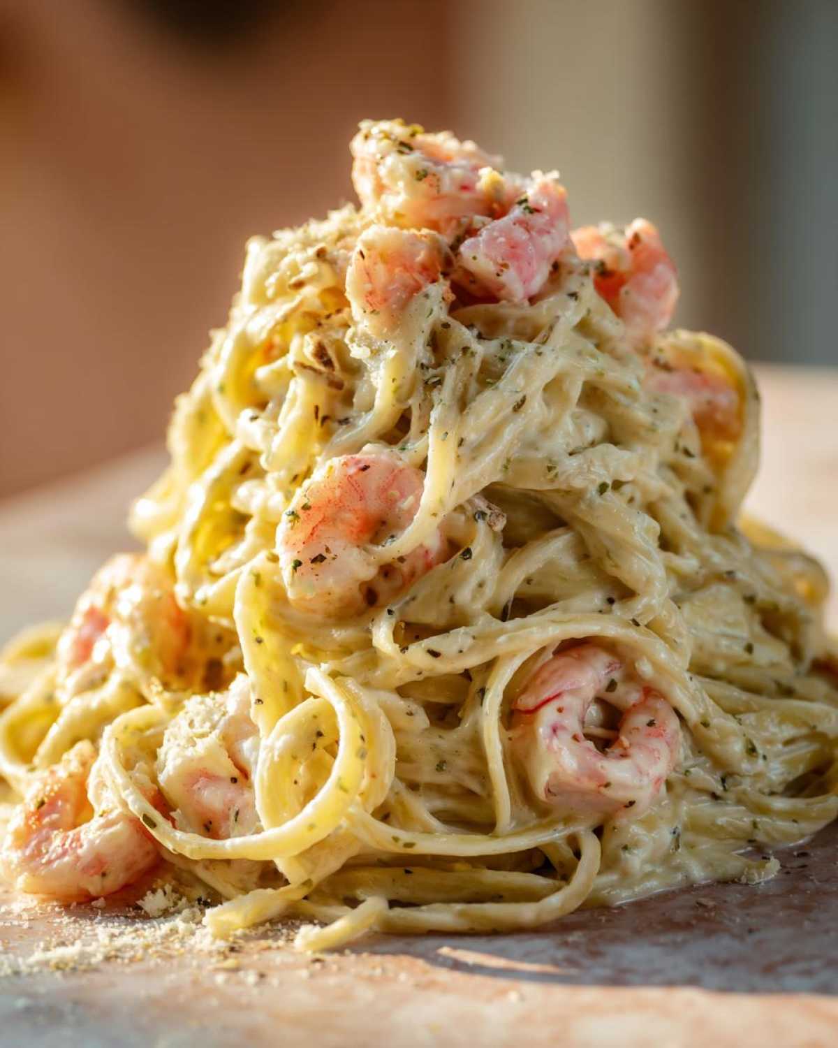 A tall mound of fettuccine tossed in rich, creamy Alfredo sauce with pink shrimp, garnished with herbs and Parmesan cheese.