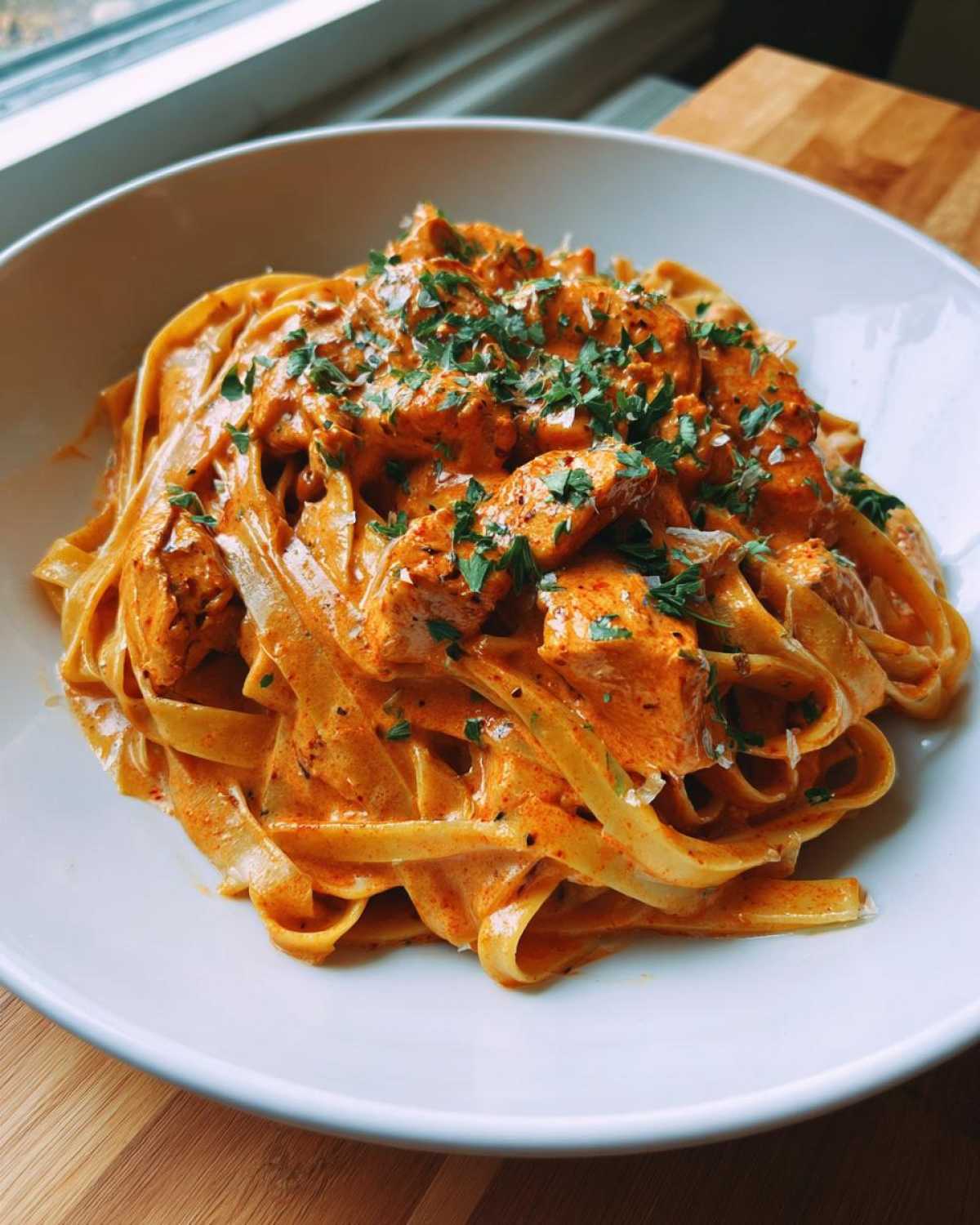 A close-up of fettuccine pasta coated in a rich, orange-hued sauce with chunks of chicken, garnished with parsley, representing Creamy Cajun Chicken Alfredo.