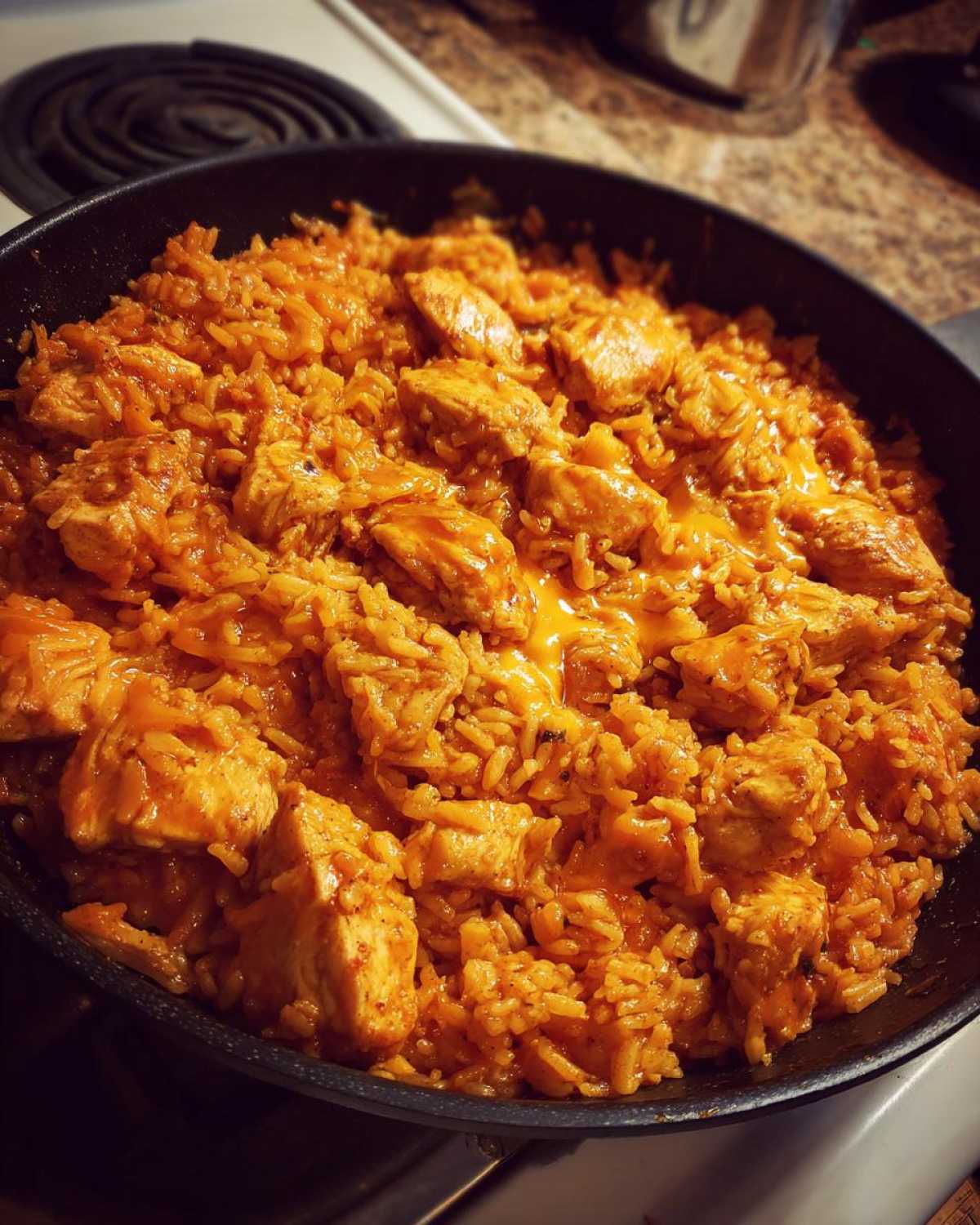 Close-up of a skillet filled with orange-hued Creamy Cajun Chicken and Rice Skillet, featuring chunks of chicken and melted cheese.