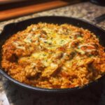 Close-up of a skillet filled with creamy Cajun Chicken and Rice Skillet, topped with melted white cheese and herbs.
