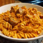 A close-up of Creamy Cajun Chicken Pasta featuring rotini/fusilli pasta coated in a rich, orange-hued sauce with chunks of seasoned chicken.