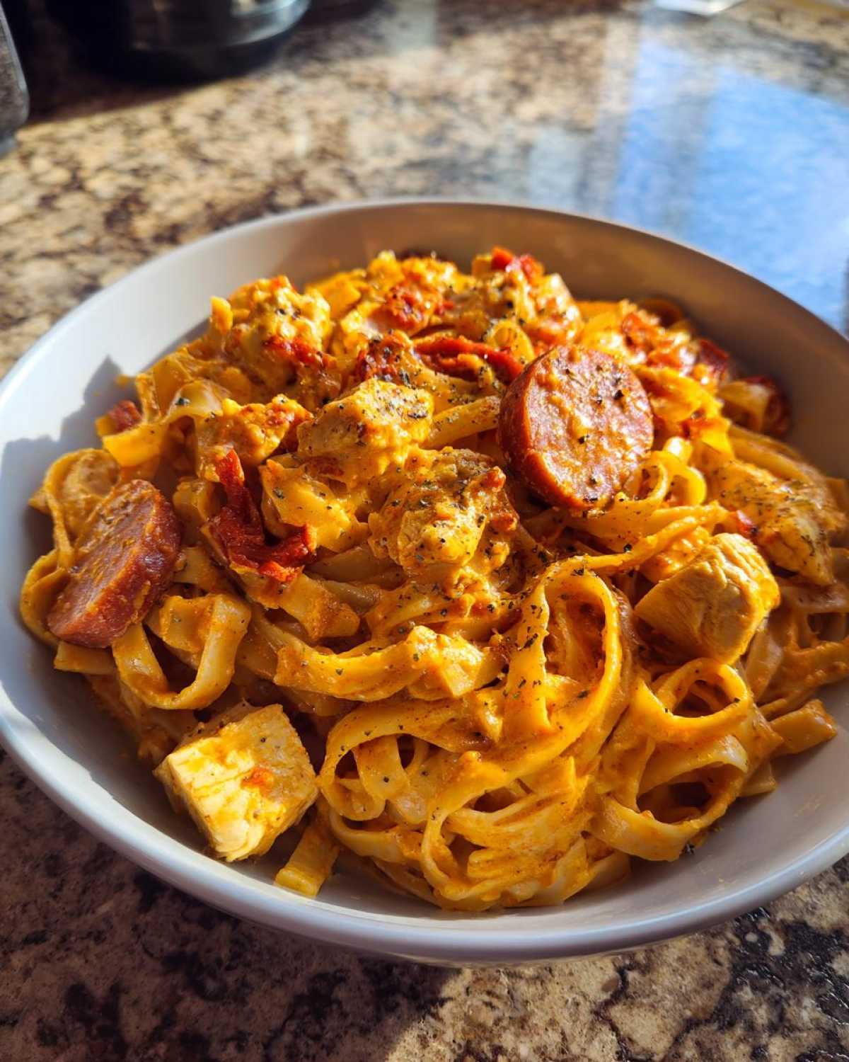 Close-up of a bowl of Creamy Cajun Chicken Pasta with fettuccine, chunks of chicken, and slices of smoked sausage.
