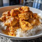 Close-up of tender chicken pieces coated in a rich, orange Creamy Cajun Chicken Skillet sauce served over white rice in a bowl.