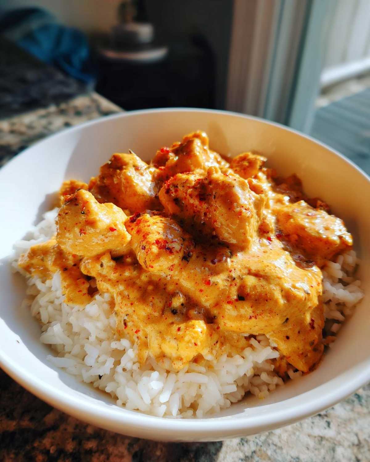 A white bowl filled with white rice topped with creamy Cajun chicken skillet pieces coated in a rich, orange sauce.