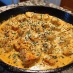 Close-up of Creamy Cajun Chicken Skillet, featuring seasoned chicken pieces swimming in a rich, orange-hued cream sauce, topped with herbs.