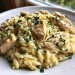 A close-up of a serving of Creamy Garlic Parmesan Orzo with Chicken topped with fresh parsley.