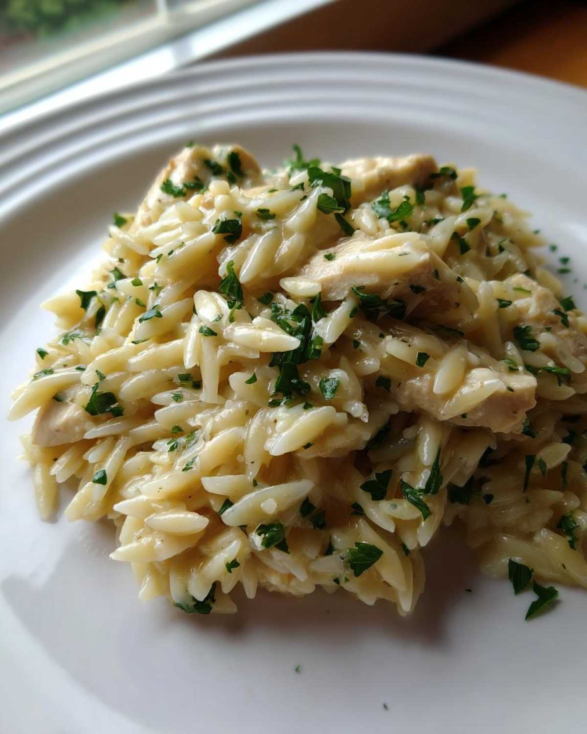 A close-up of creamy garlic parmesan orzo with chicken, topped with fresh chopped parsley on a white plate.