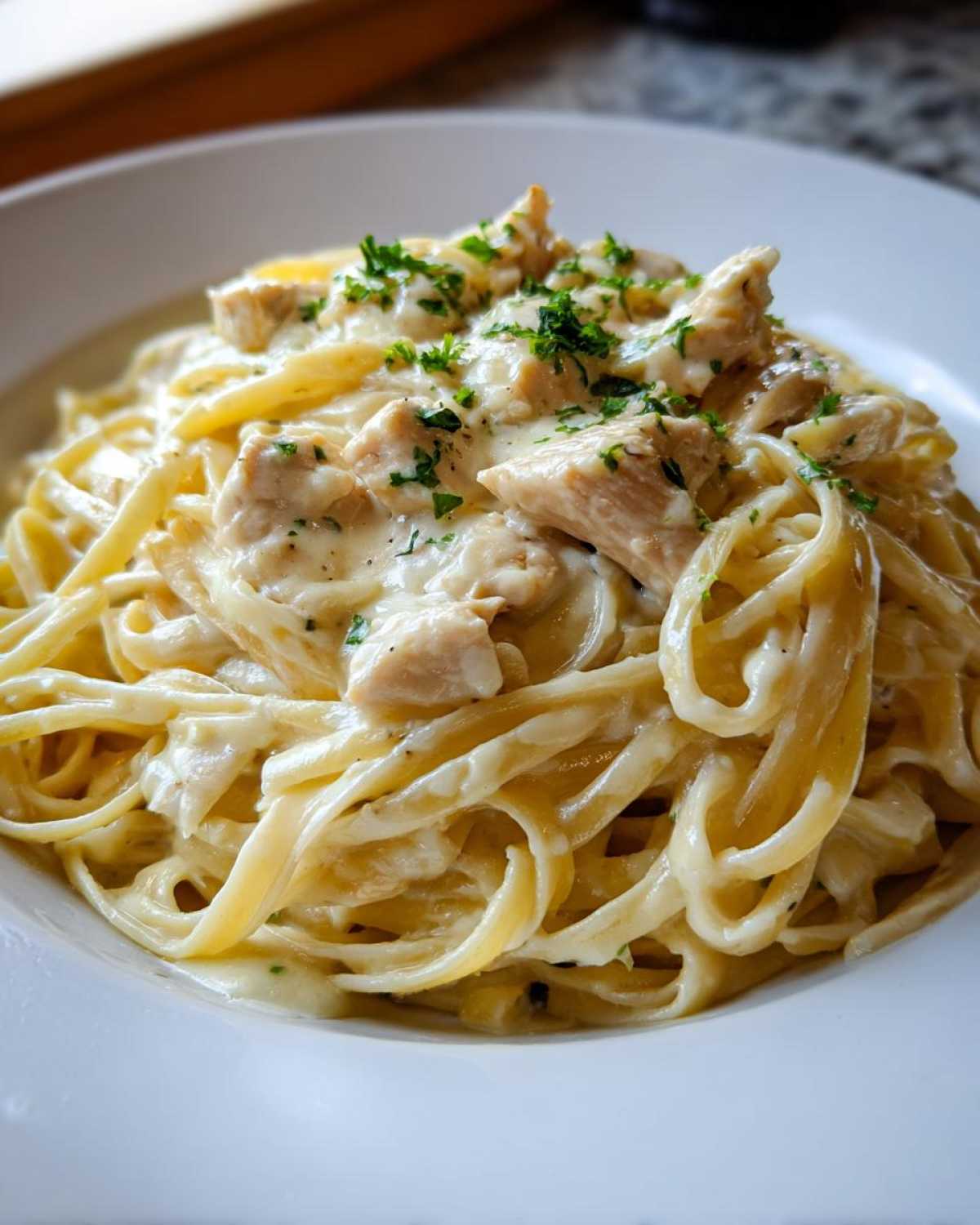 Close-up of Creamy Lemon Chicken Pasta featuring fettuccine coated in a rich sauce with chunks of chicken and fresh parsley.