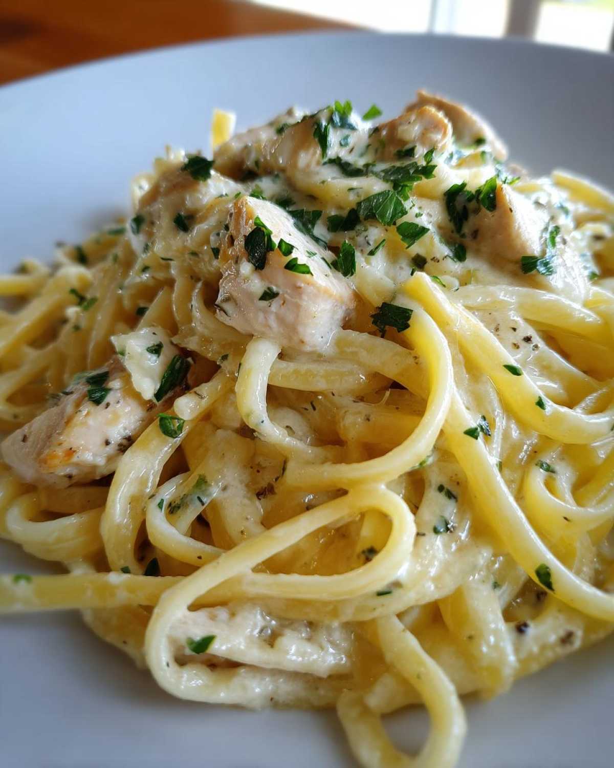A close-up view of a serving of Creamy Lemon Chicken Pasta, featuring linguine coated in a light sauce, topped with diced chicken and fresh parsley.