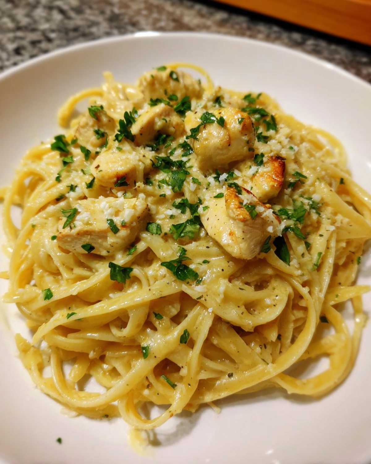 Close-up of a bowl of Creamy Lemon Chicken Pasta tossed in a light sauce, topped with diced chicken and fresh parsley.