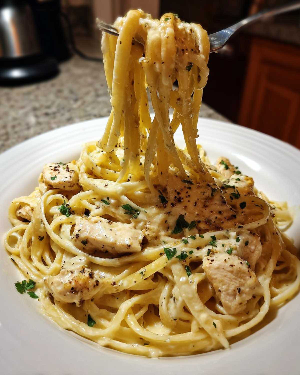 A fork lifts linguine noodles coated in a creamy sauce, mixed with chunks of seasoned chicken from the Creamy Lemon Chicken Pasta.