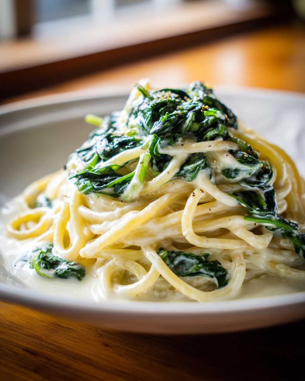 Close-up of spaghetti coated in a creamy sauce, topped with wilted spinach for Creamy Lemon Ricotta Pasta.