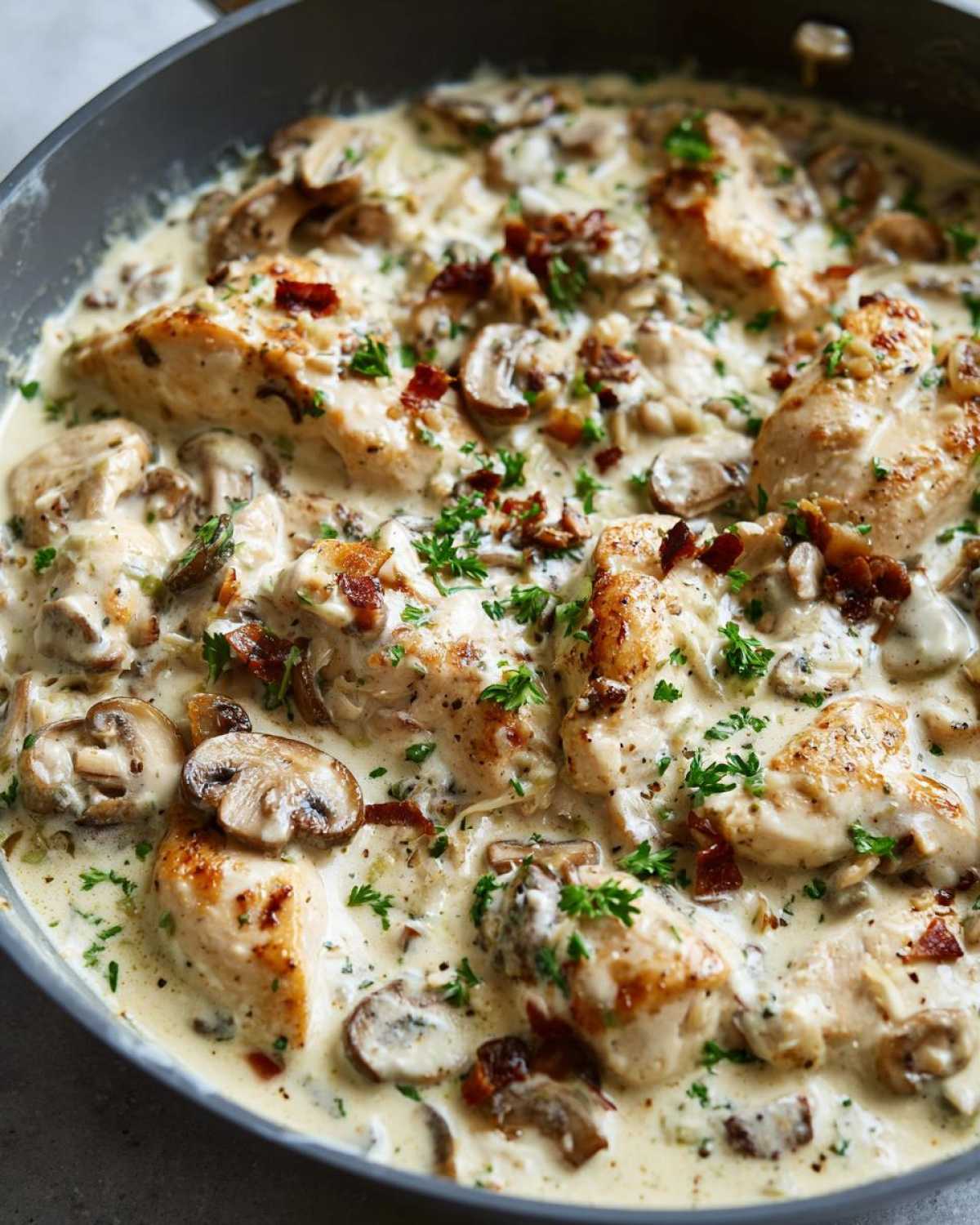 Close-up of seared chicken breasts smothered in a rich Creamy Mushroom Alfredo Chicken Skillet sauce with sliced mushrooms and parsley.