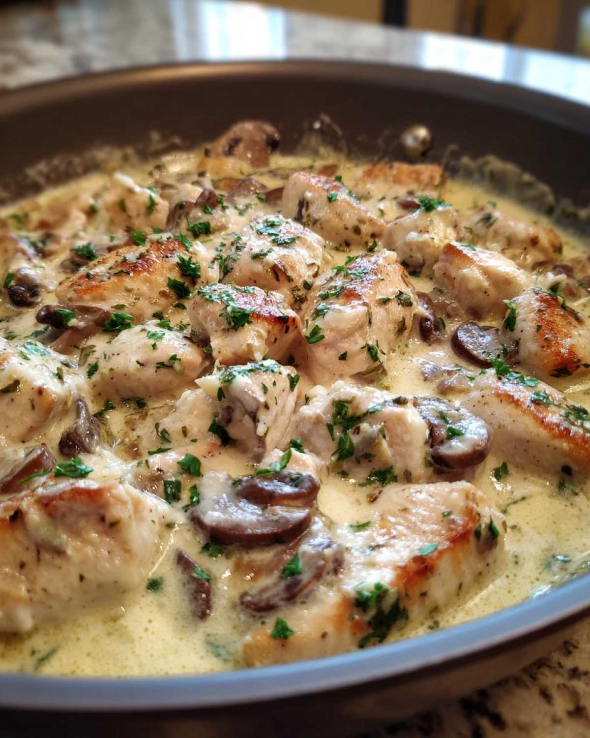 Close-up of seared chicken pieces and sliced mushrooms simmering in a rich Creamy Mushroom Alfredo Chicken Skillet sauce, garnished with parsley.