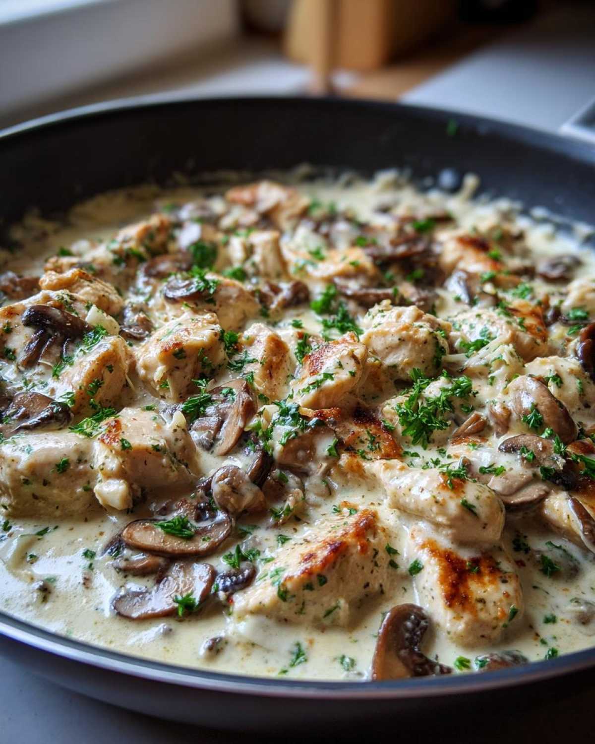 Close-up of seared chicken pieces and sliced mushrooms coated in a rich, creamy sauce in a black skillet, garnished with parsley for Creamy Mushroom Alfredo Chicken Skillet.