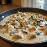 Close-up of chunks of chicken and sliced mushrooms simmering in a rich, creamy sauce in a skillet, garnished with parsley, for Creamy Mushroom Alfredo Chicken Skillet.