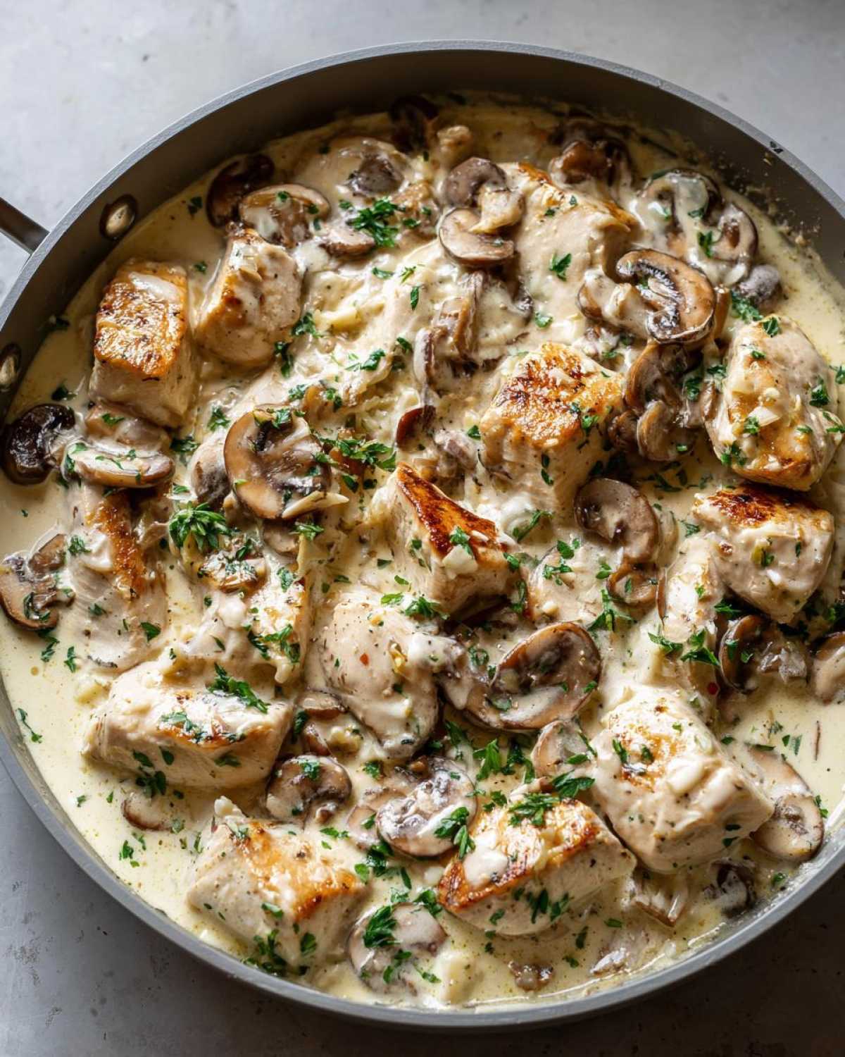 Close-up of seared chicken pieces and sliced mushrooms coated in a rich, creamy sauce in a skillet, making the Creamy Mushroom Alfredo Chicken Skillet.