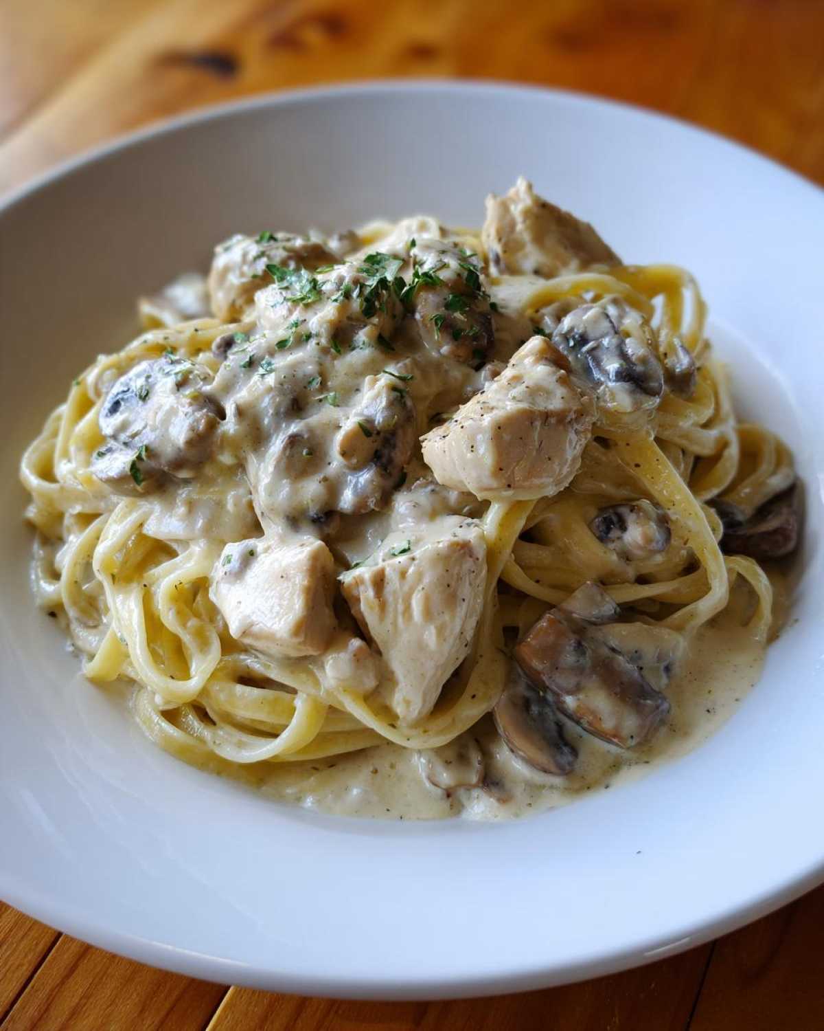 A close-up of a white bowl filled with Creamy Mushroom Chicken Alfredo Pasta, topped with parsley.