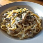 A close-up serving of rich Creamy Mushroom Chicken Alfredo Pasta with fettuccine, chicken pieces, mushrooms, and parsley garnish.