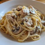 A close-up of rich Creamy Mushroom Chicken Alfredo Pasta tossed in a white bowl.
