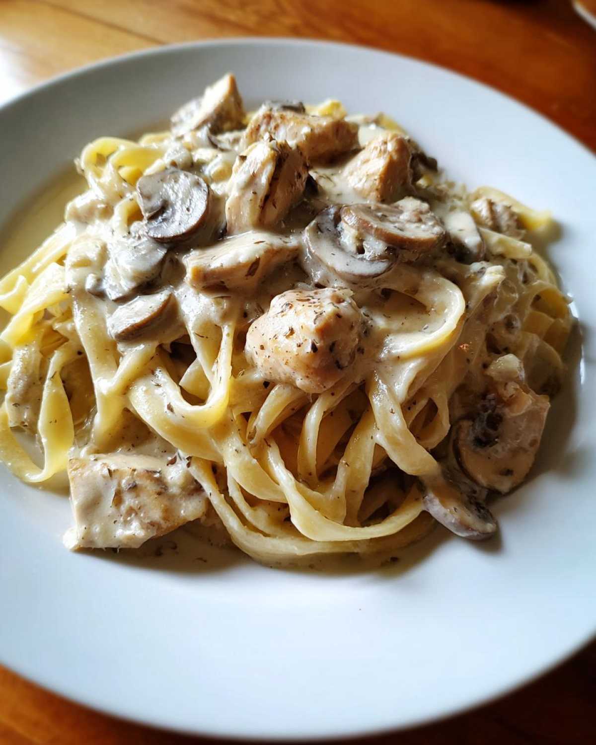 A close-up of a white plate filled with fettuccine pasta tossed in a rich sauce with chunks of chicken and sliced mushrooms, representing Creamy Mushroom Chicken Alfredo Pasta.