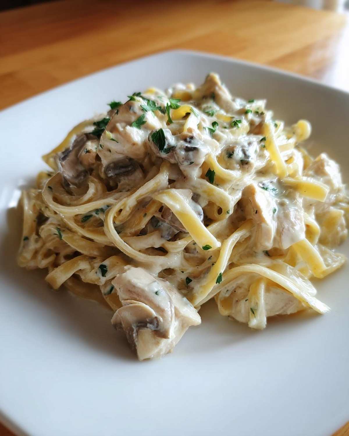A close-up of a serving of Creamy Mushroom Chicken Alfredo Pasta with fettuccine, chicken pieces, mushrooms, and parsley garnish.