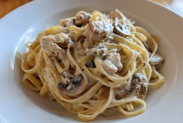 A close-up of rich Creamy Mushroom Chicken Alfredo Pasta tossed in a white bowl.