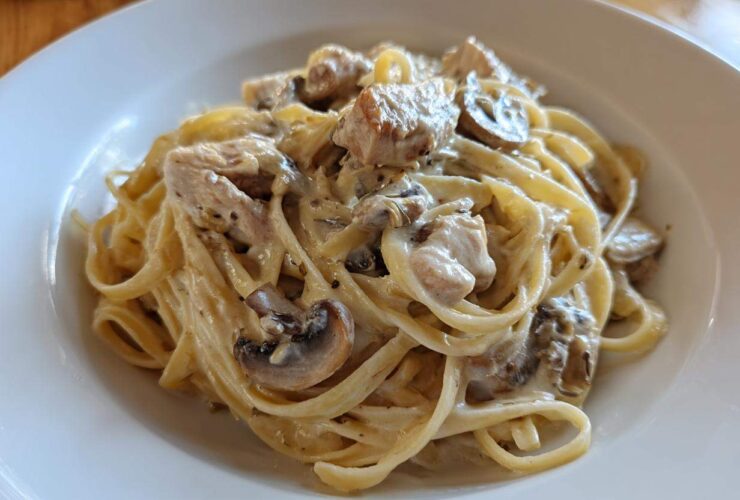 A close-up of rich Creamy Mushroom Chicken Alfredo Pasta tossed in a white bowl.