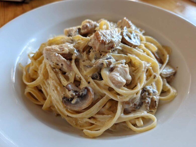 A close-up of rich Creamy Mushroom Chicken Alfredo Pasta tossed in a white bowl.