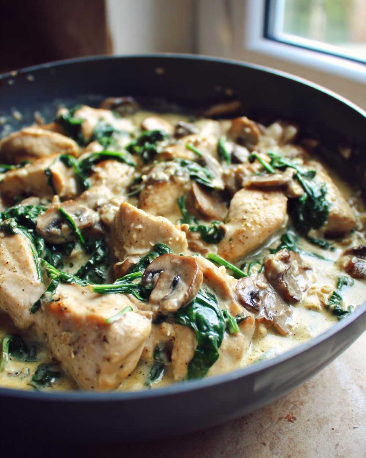 Close-up of tender chicken pieces in a rich, creamy sauce with sautéed mushrooms and wilted spinach, part of the Creamy Mushroom and Spinach Chicken Skillet.