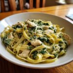Close-up of a white bowl filled with Creamy Spinach Pasta with Chicken Dinner, topped with grated Parmesan cheese.