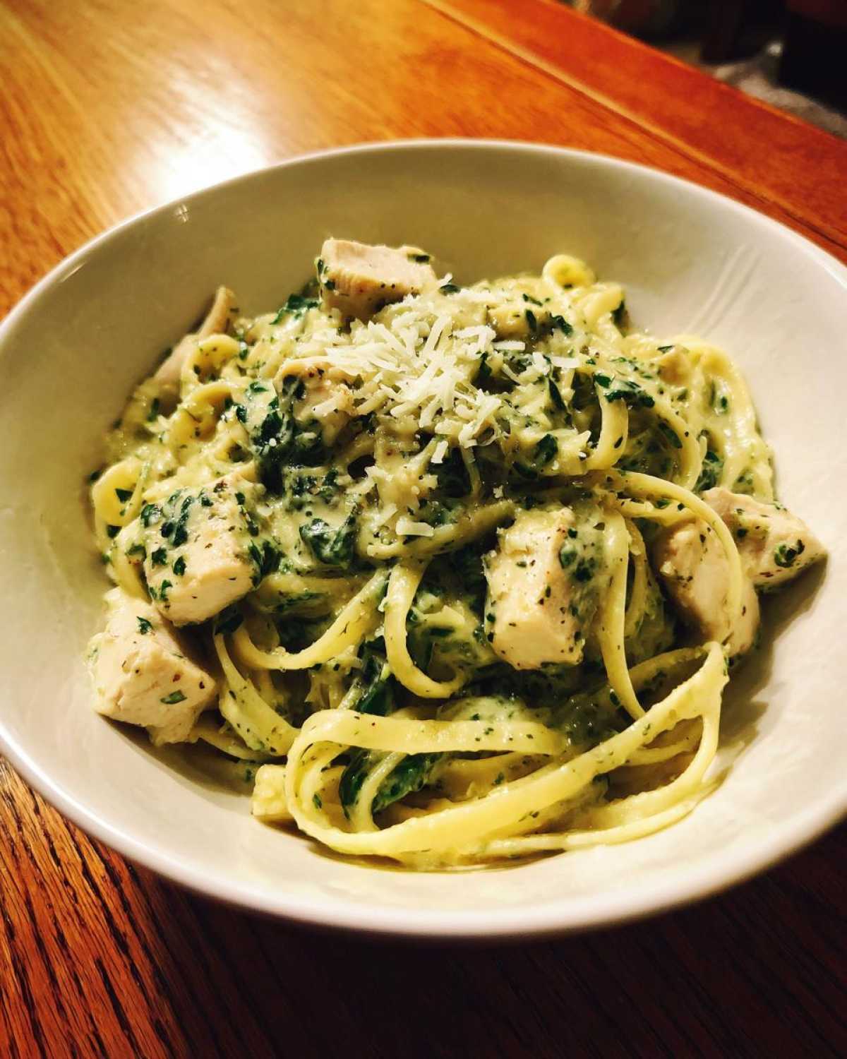 A close-up of a bowl of Creamy Spinach Pasta with Chicken Dinner, topped with grated Parmesan cheese.