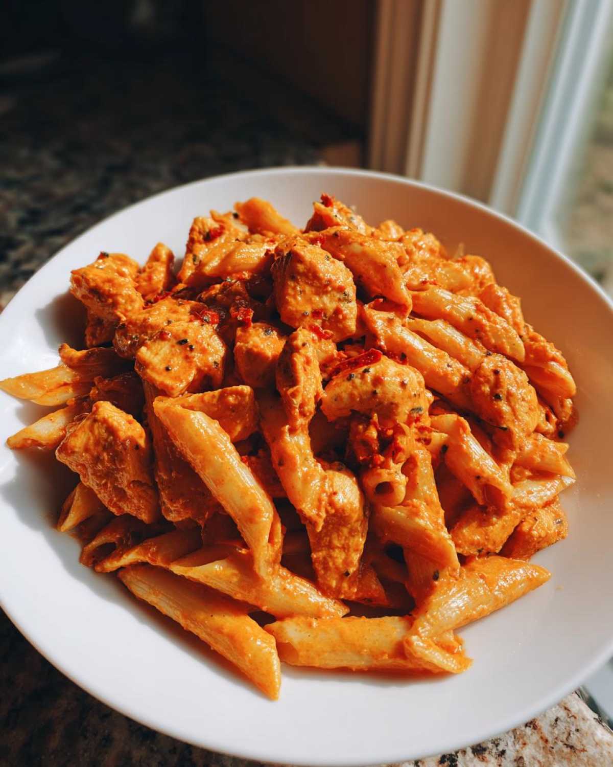 A white bowl filled with Creamy Sun Dried Tomato Pasta with Chicken, coated in a rich orange sauce.