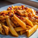 Close-up of penne pasta coated in a rich sauce with chicken pieces and sun dried tomatoes in Creamy Sun Dried Tomato Pasta with Chicken.