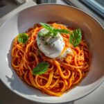 A bowl of vibrant Creamy Tomato Pasta with Burrata Cheese topped with fresh basil leaves.