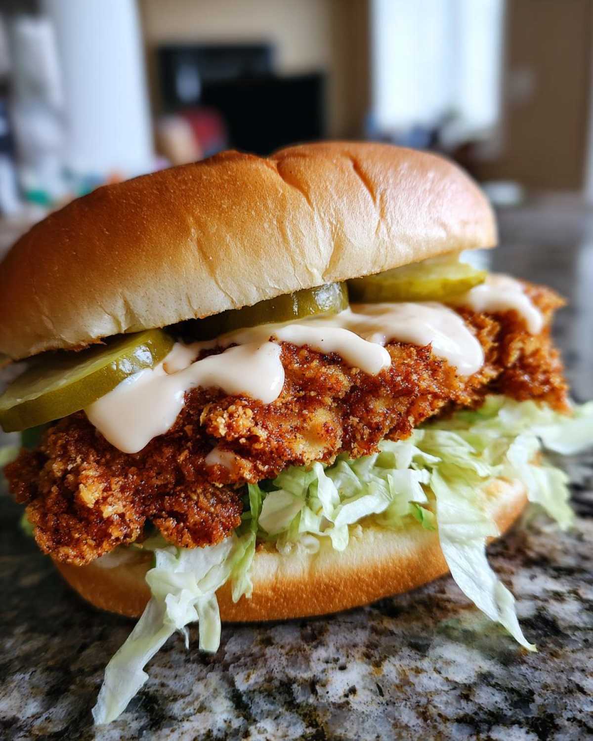 A close-up view of a Crispy Chicken Sandwich with Garlic Sauce, featuring a thick fried patty, pickles, and shredded lettuce on a soft bun.