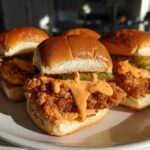 A close-up of four Crispy Chicken Sliders with Spicy Mayo and pickles served on a white plate.