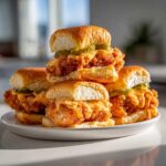A stack of four Crispy Chicken Sliders with Spicy Mayo and pickles served on a white plate.