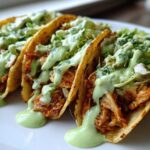 Three Crispy Chicken Tacos loaded with shredded chicken, lettuce, and drizzled generously with avocado cream sauce.