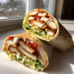 Close-up of a Crispy Chicken Wrap with Creamy Garlic Sauce, cut in half showing layers of fried chicken, lettuce, and tomato.