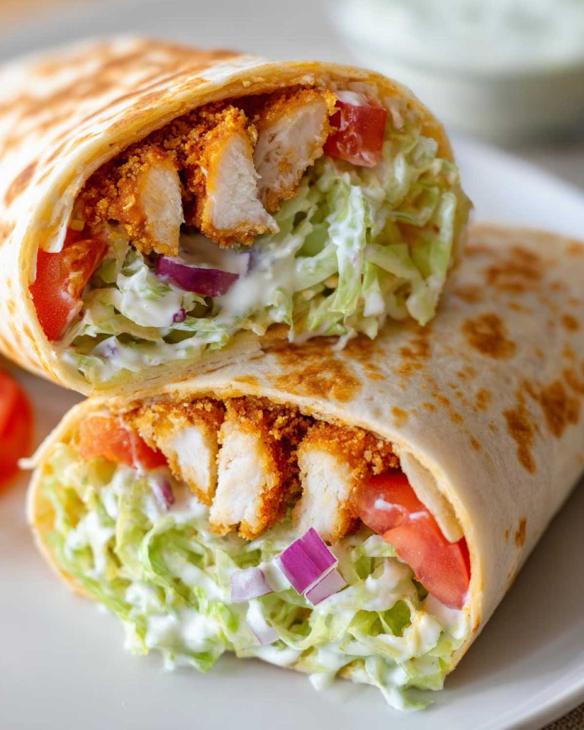 Cross-section of a Crispy Chicken Wrap with Creamy Ranch Sauce showing breaded chicken, lettuce, tomato, and onion.