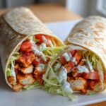 Two halves of a Crispy Chicken Wrap with Creamy Ranch Sauce, showing seasoned chicken, lettuce, and tomatoes.