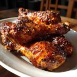 A close-up of several glossy Crispy Honey Garlic Chicken Drumsticks Oven Baked piled on a white plate.