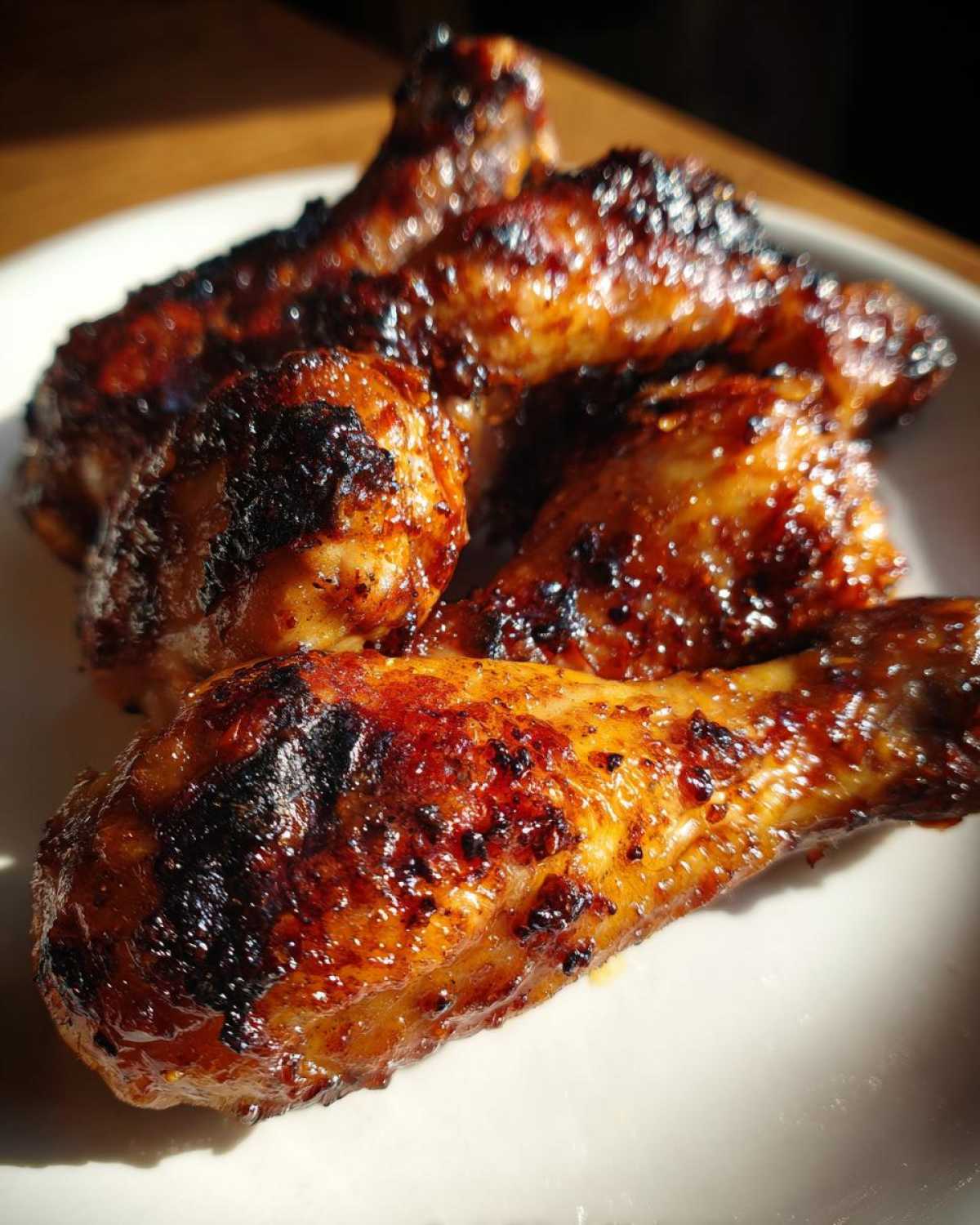 Close-up of several glossy, caramelized Crispy Honey Garlic Chicken Drumsticks Oven Baked on a white plate.