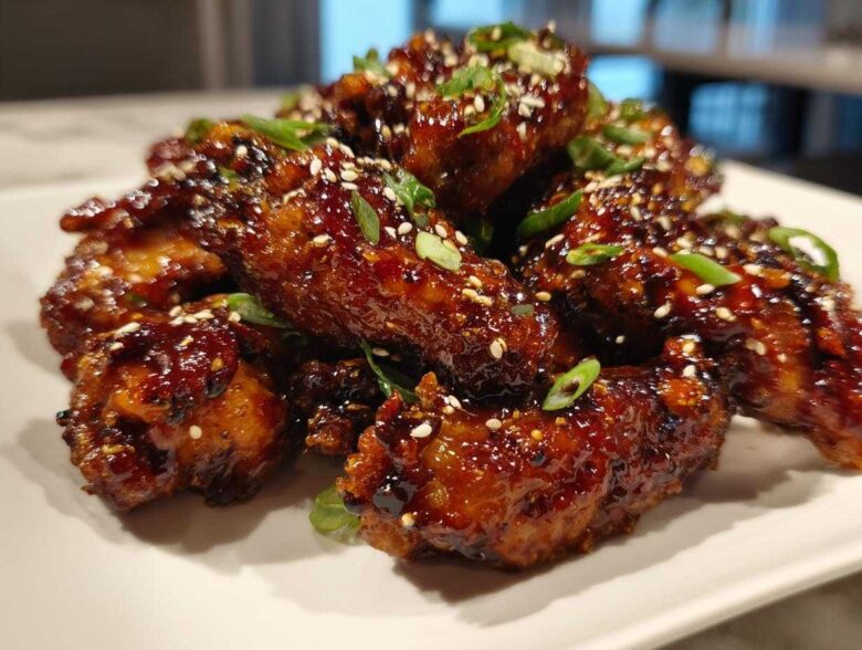 A mound of oven-baked Sticky Teriyaki Chicken Wings, glazed and garnished with sesame seeds and green onions.
