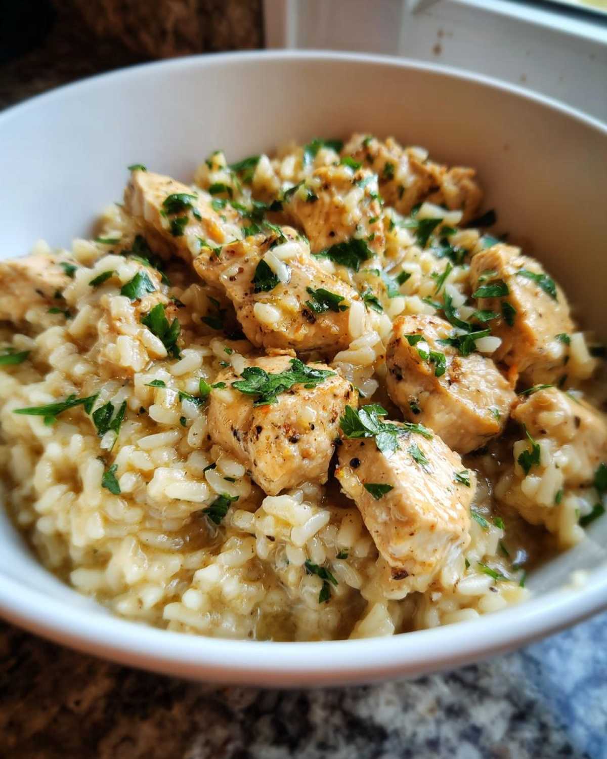 Close-up of creamy Garlic Butter Chicken and Rice Dinner topped with fresh parsley in a white bowl.
